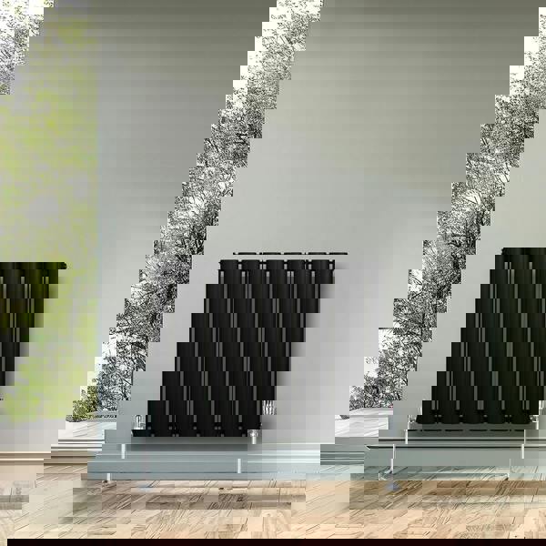 Sleek black oval single column radiator, 600 x 780mm, mounted on a light gray wall, complemented by modern chrome valves and a natural backdrop