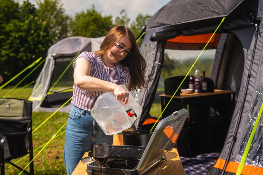 a woman fills a pot on a camping stove in front of the  Loopo Breeze® v2 Inflatable Campervan Awning OLPRO imageset:Charcoal