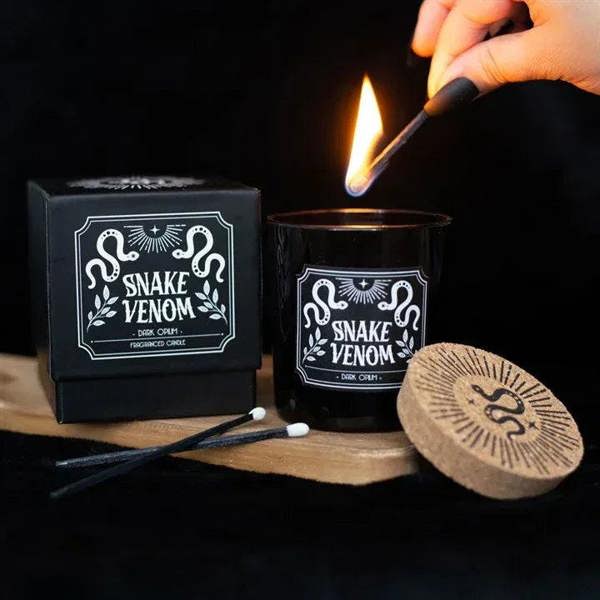 Lit black jar Snake Venom candle with cork lid and white label; match held above