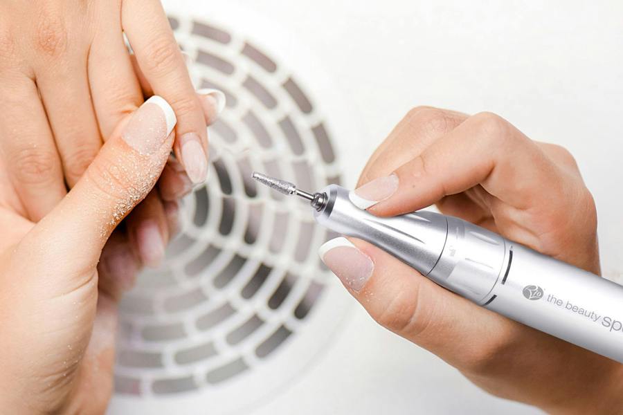 Motorized nail file being used in salon to file down acrylic manicure, electric nail filing finger nails