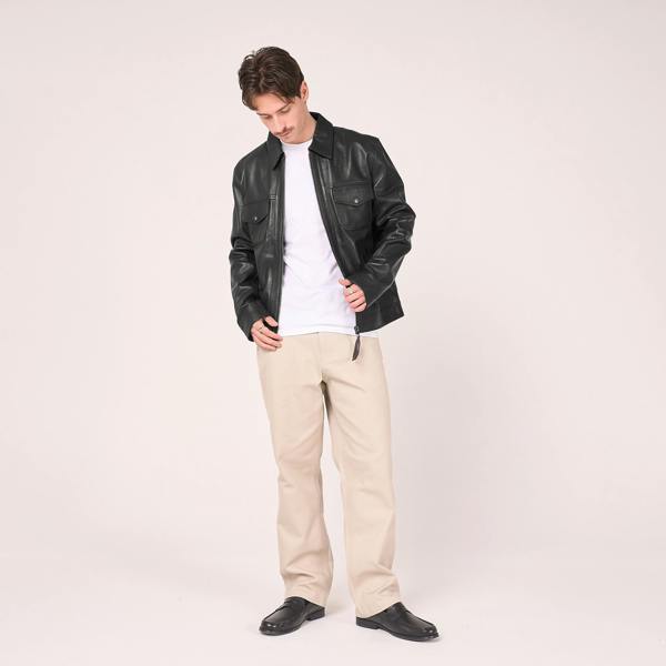Full outfit shown: Man in photography studio poses in a leather jacket open to show a white t-shirt and cream smart/casual trousers.