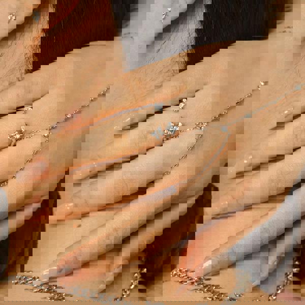 Close-up of a hand wearing silver rings and a necklace with a blurred background. Bloomtine-Enchanting-Flutterfly-ring. A professional-hero-shot of a dainty-925-sterling-silver-butterfly-ring featuring four-scintillating-moissanite-gemstones on a-white-background. This-hand-polished-piece showcases the-brilliant-light-refraction of the-sustainable-moissanites and the-intricate-butterfly-motif, representing-spiritual-transformation and effortless-beauty