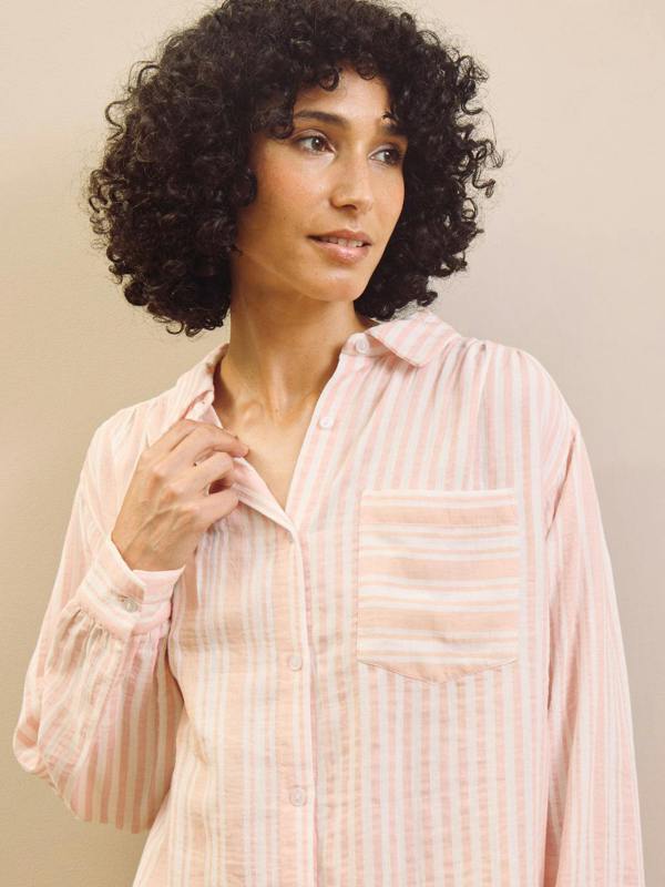 Woman wearing a light pink striped pyjama shirt against a beige background