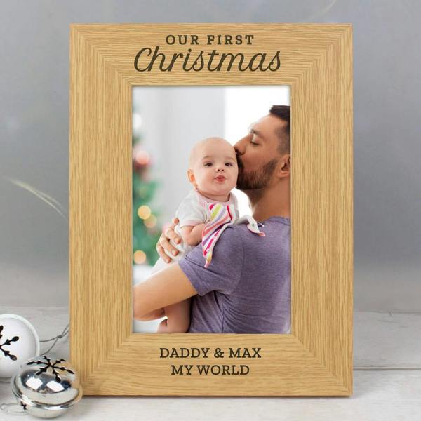 An oak veneer photo frame reading Our First Christmas and Daddy and Max My World with a photo of a dad kissing a baby.