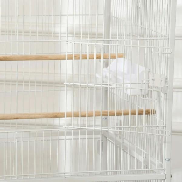 White bird cage interior with wooden perch and hanging feeder cup