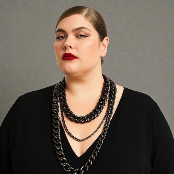 Plus Size Woman wearing a black top and a tree tiered black aluminium and metal chain necklace a against a plain background