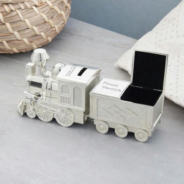 An engraved silver-plated train money box with the First Curl compartment open to show a soft, black velvet-lined interior on a grey surface.