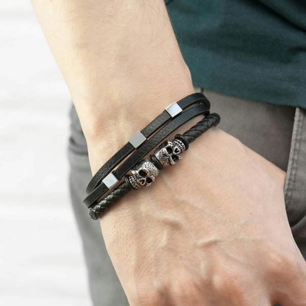 A close-up of a man's wrist wearing the black multi-strand Personalised Men's Skulls Leather Rope Bracelet with silver skull charms and square accents.
