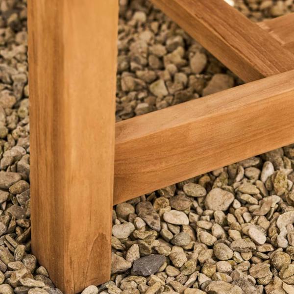 Detail of a square-cut solid teak table leg resting on a light-colored gravel garden surface.