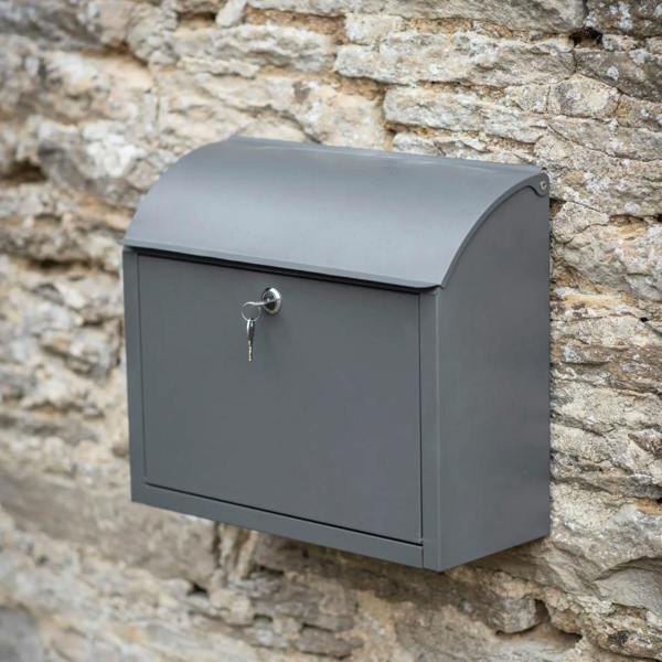 A charcoal grey metal parcel box mounted on a cream wooden wall with a secure lock and handle.
