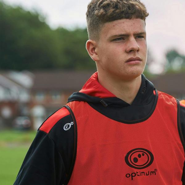 Young player in red Optimum training bib with black logo print outdoors, close-up lifestyle shot - Optimum