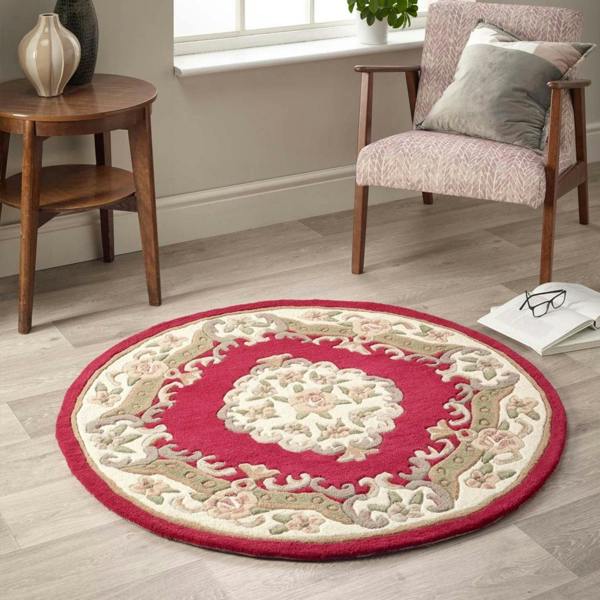 Round decorative rug with intricate patterns on a wooden floor, with a chair and side table in the background.