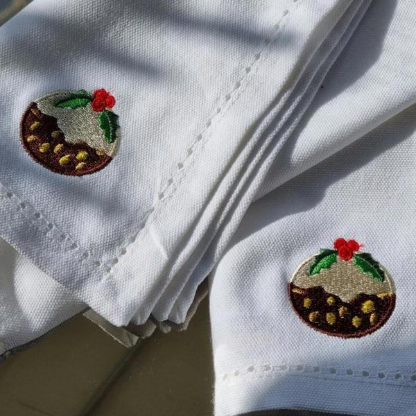 Close-up of white 100% cotton napkins featuring an embroidered Christmas pudding motif with sparkly gold details.