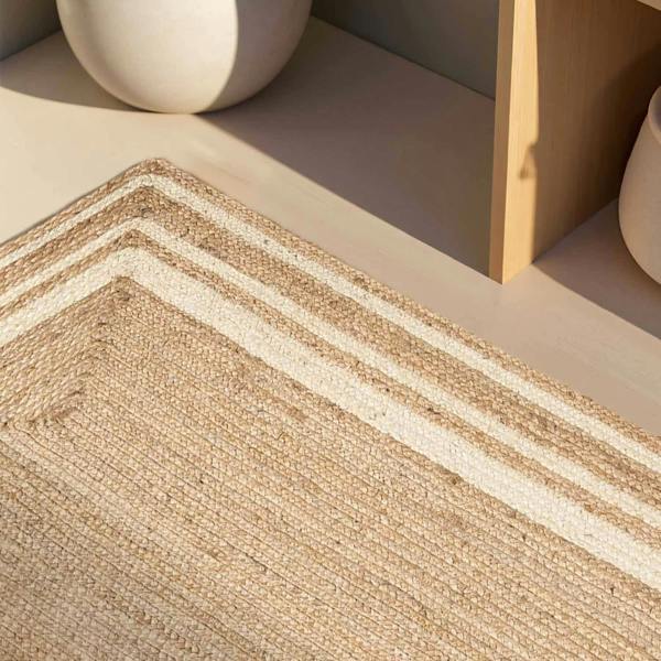 Close-up of a woven jute rug with a geometric pattern on a neutral background.