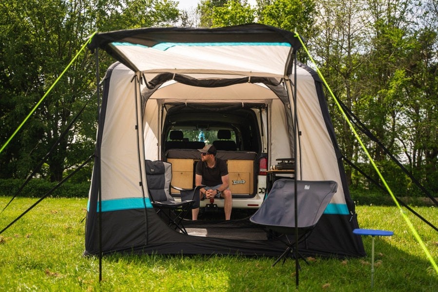 A man sits inside on the bumper of his campervan in the tunnel of a Snug Inflatable Tailgate Awning