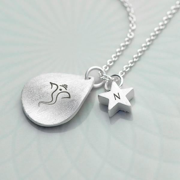 Silver petal necklace engraved with Ganesh and a star charm engraved with the letter N on a white surface