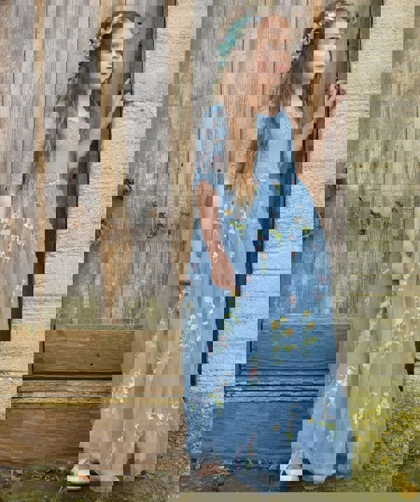 Young girl in a blue floral dress standing against a wooden wall.
