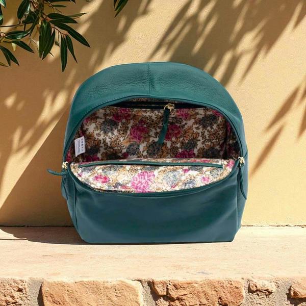 Teal backpack with floral interior on a stone surface against a beige wall.