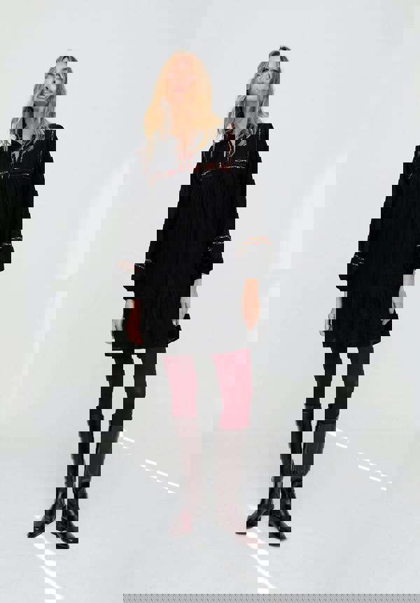 Woman wearing a black dress with red embroidery and dark boots on a white background