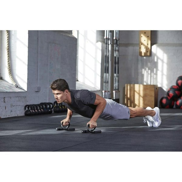 Man performing push-ups with black adidas push up stands on a gym floor.