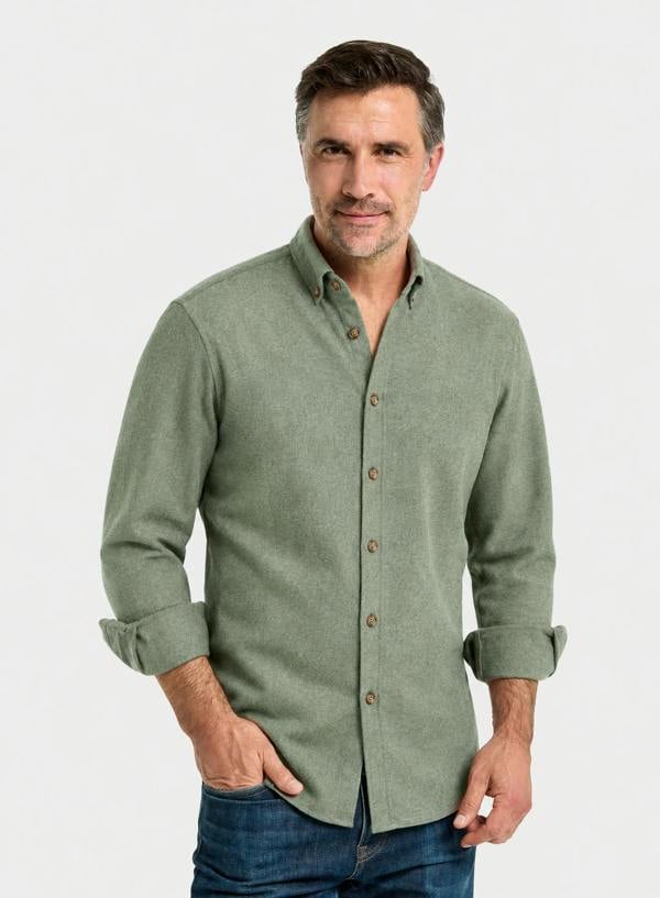 A man wearing a sage green long-sleeve button-down shirt with rolled-up sleeves and blue jeans, standing against a light gray studio background.