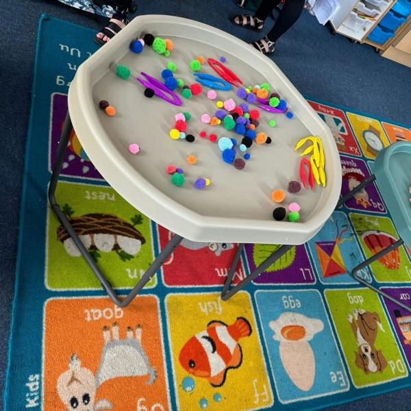 90cm plastic activity tables with gray metal legs in a classroom setting, filled with colorful toys and blocks, set on a colorful alphabet rug.