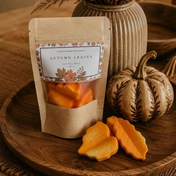 Autumn Leaves soy wax melts shaped like leaves next to a kraft paper pouch on a wooden tray with a decorative pumpkin by Abode Home & Gifts