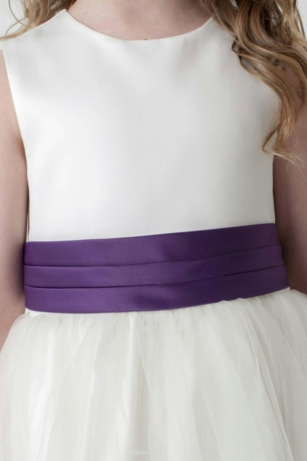 Close up of Ivory dress with a purple belt worn by a child