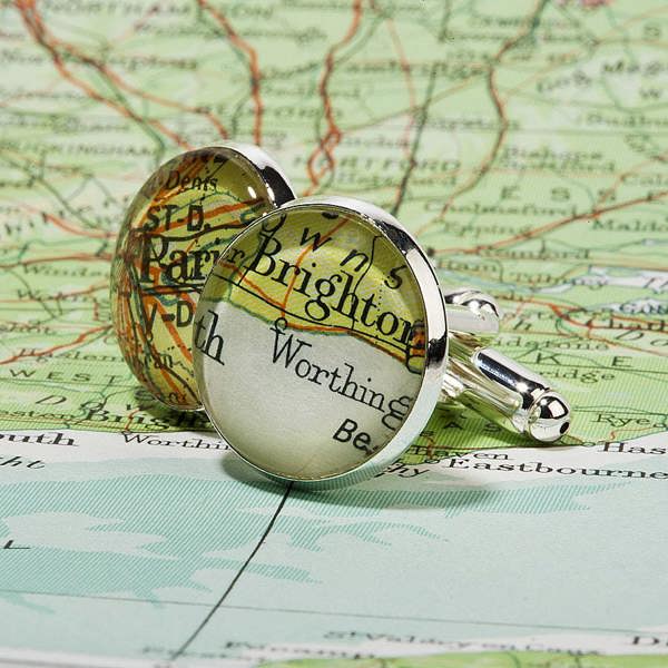 Two silver plated round cufflinks featuring vintage maps of Brighton and Worthing, displayed on top of a detailed green and cream road map.