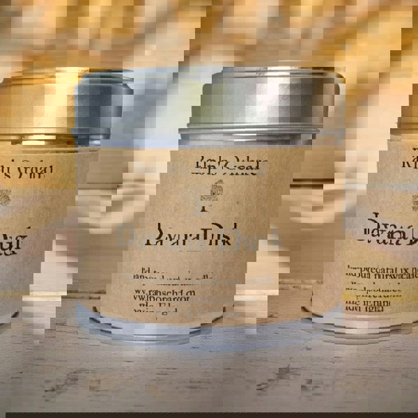 Candle in a tin labeled 'Davana Dusk' by Ralph's Orchard on a wooden surface.