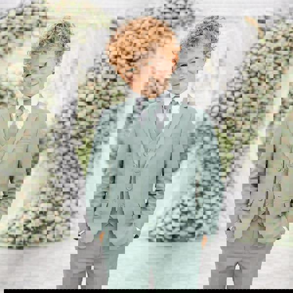 Young boy in a light blue suit standing in front of floral decorations