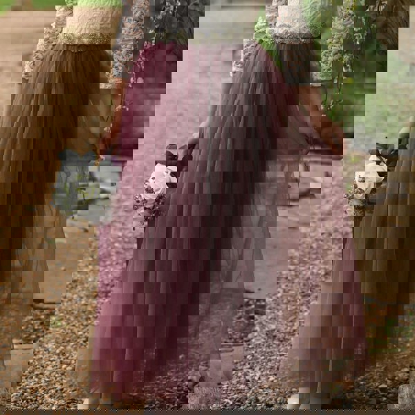 Person wearing a white lace top and purple tulle skirt holding a bouquet outdoors.