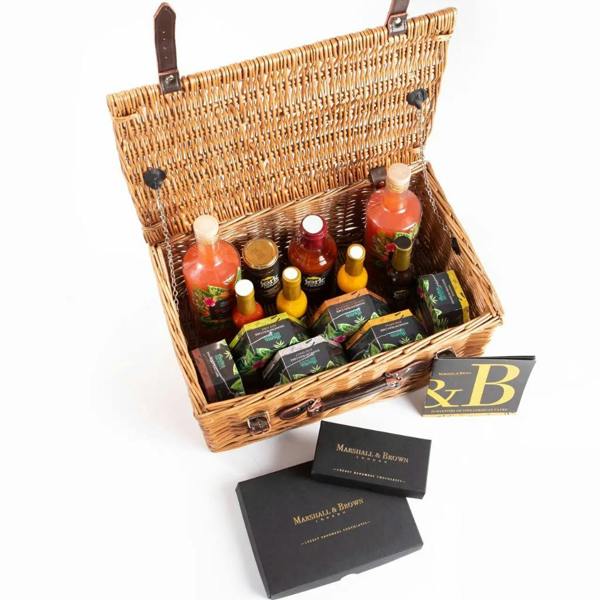 Overhead view of an open traditional wicker hamper filled with rum cakes, spicy jerk sauces, rum punch, and artisan chocolates.
