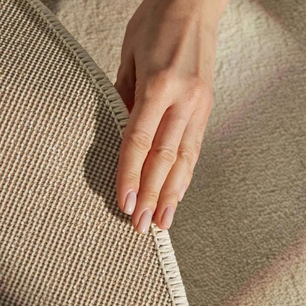 Hand touching the edge of a textured beige fabric
