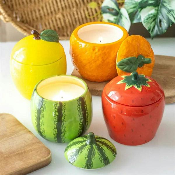 Assorted fruit-shaped candle jars: green watermelon, red, orange, and yellow.