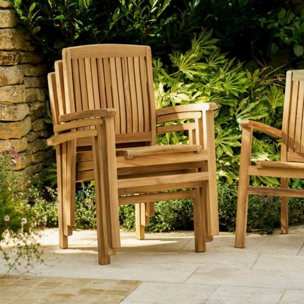 A stack of three solid teak carver armchairs showing the space-saving storage design on a stone patio.