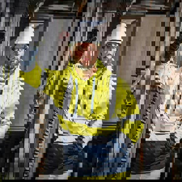 Scruffs High Visibility Mens Hi-Viz Work Pull Over Hoodie, a man wearing a bright yellow high visibility hoodie with reflective stripes and a white safety helmet in an industrial setting.