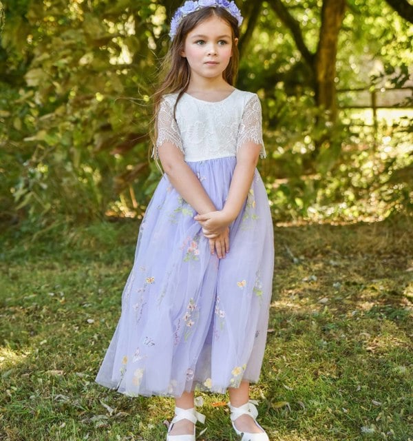 Young girl in a light purple dress with floral patterns standing outdoors.