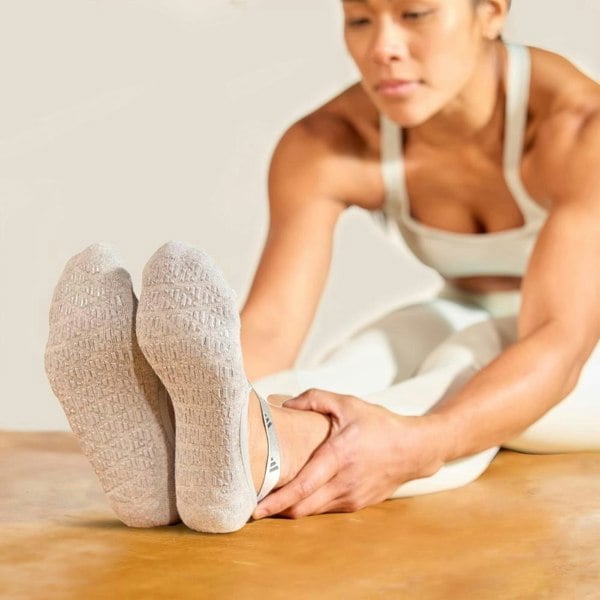 Person stretching on a wooden floor wearing grey adidas studio yoga socks.