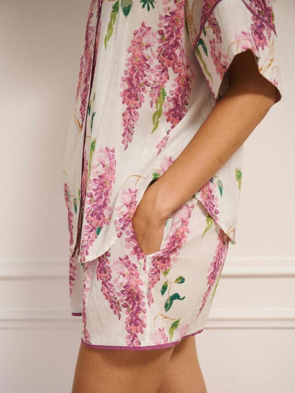 Model wearing white cotton voile oversized shortie pyjamas with pink wisteria print, short-sleeve shirt and elasticated waist shorts with pockets. side detail