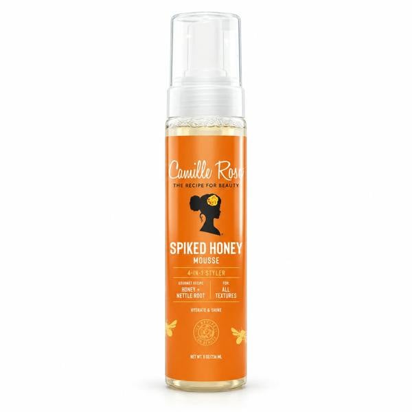 A bottle of Camille Rose Spiked Honey Mousse on a clean white background. The product features a vibrant orange label with a black silhouette of a woman's profile and yellow honey accents, topped with a clear pump dispenser.