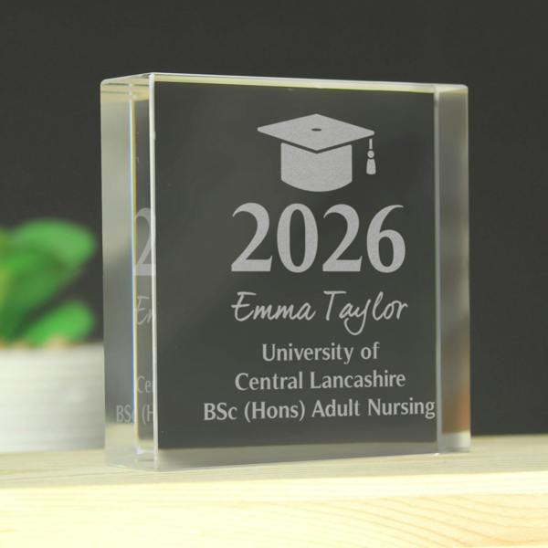 A personalised graduation crystal token engraved with the name Emma Taylor, the year 2026, and a BSc (Hons) Adult Nursing degree from the University of Central Lancashire, resting on a wooden shelf.