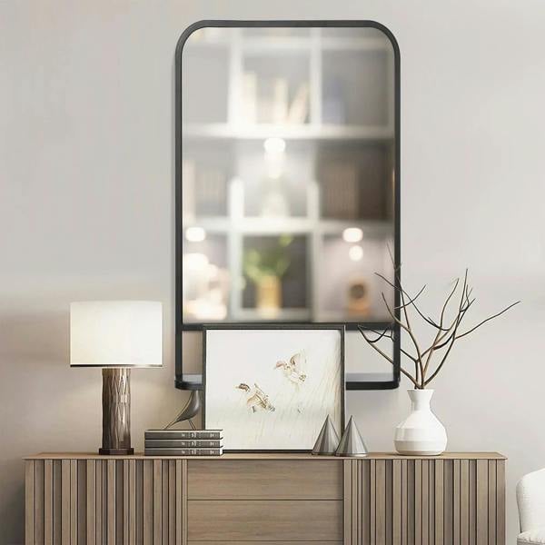 Black wall mirror with rounded top frame and storage rail below