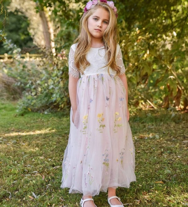 Young girl in a floral dress standing in a natural setting with greenery.