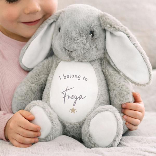 A young child hugging a soft grey plush rabbit titled Personalised I Belong To Bunny, custom printed with the name Freya and a small gold star on its white belly.