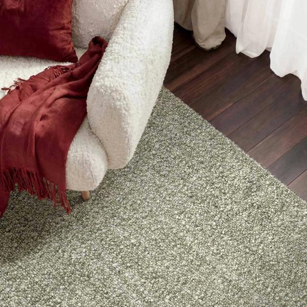 Close-up of a textured green carpet with a white couch and red blanket in the background.