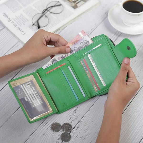 Green wallet with money and cards on a wooden surface with a cup of coffee and glasses.