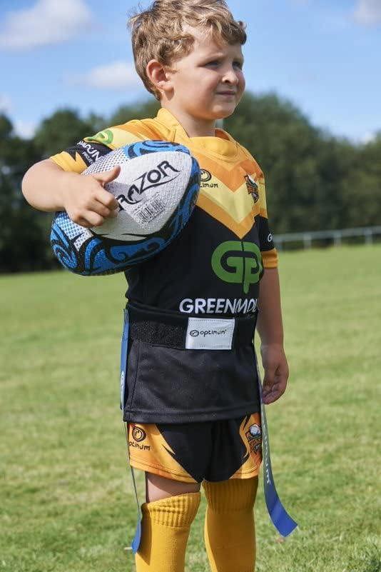 Young rugby player standing with a ball wearing blue Optimum tag belt over orange and black kit, on grass
