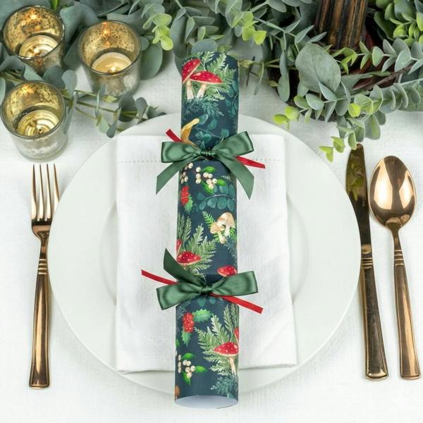 Six dark green Christmas crackers with a toadstool pattern on a decorated festive dinner table.