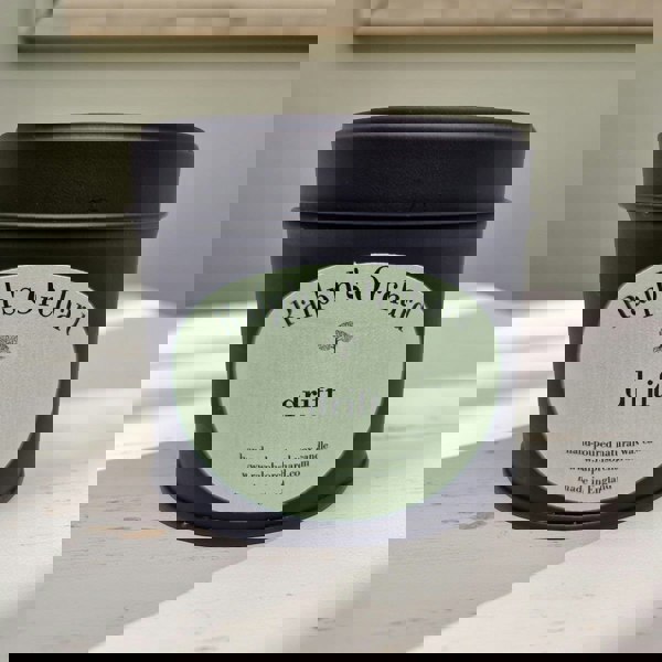 Candle in a black tin with 'Ralph's Orchard' label on a light wooden surface.